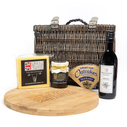 Gourmet gift set with a basket, cheese, jam, oatcakes, and wine on a white background